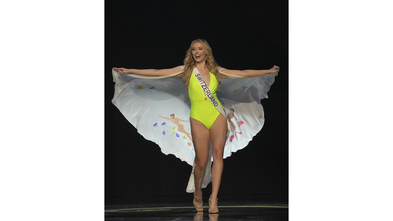 Smiling blonde in yellow bathing suit and white cape.