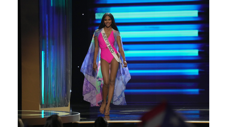 Dark-skinned brunette in pink swimsuit and lavender cape.