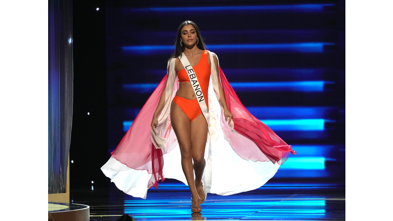 Brunette in orange swimsuit and white and red cape.