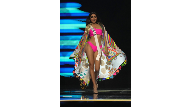 Brunette in pink swimsuit and multi-colored cape.
