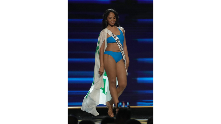 Dark-skinned brunette in blue swimsuit and white cape.