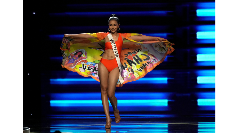 Dark-skinned brunette in orange swimsuit and multi-colored printed cape.