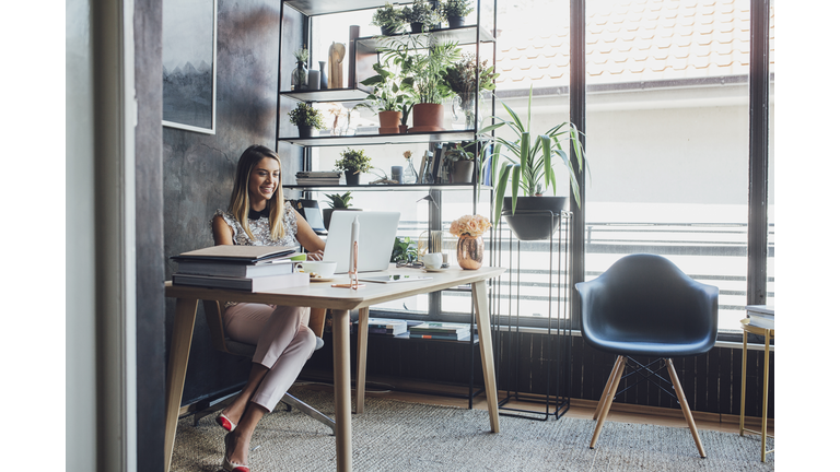 Happy businesswoman working on laptop computer while sitting at table in home office