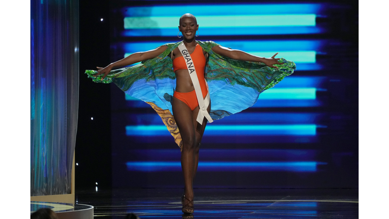 Dark-skinned woman in orange swimsuit and green cape.