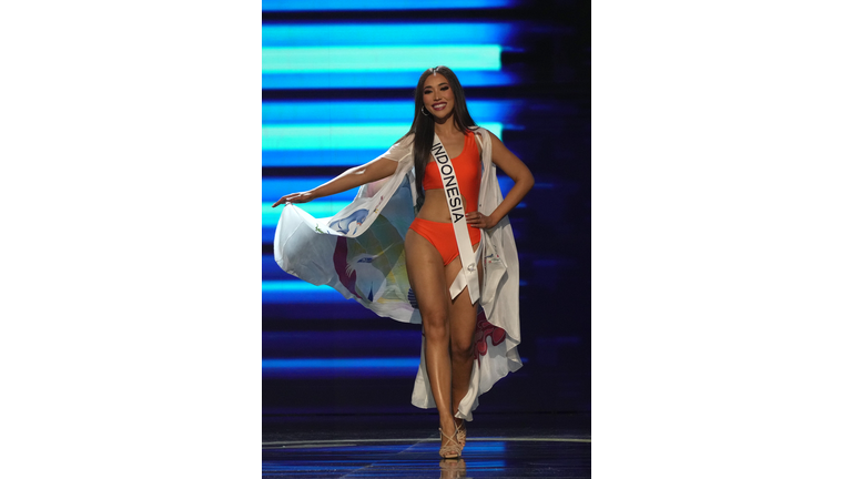 Smiling brunette in orange swimsuit and multi-colored cape.