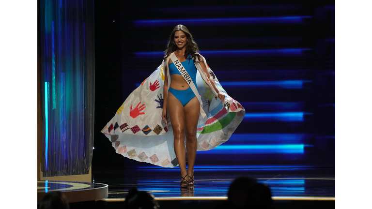 Brunette in blue swimsuit and white cape with handprints and patterns along the border.