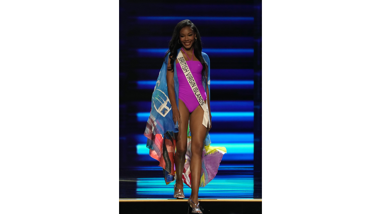 Dark-skinned brunette in purple one-piece swimsuit and multi-colored cape.