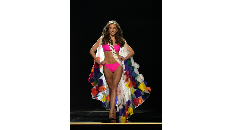 Brunette in pink swimsuit and white cape with multicolored blocks along the border.