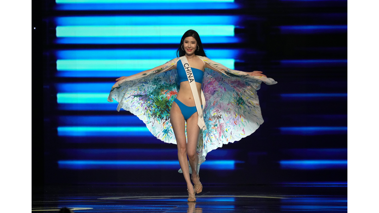 Very thin Asian brunette in blue swimsuit and multi-colored cape.