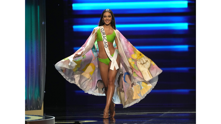 Brunette in green swimsuit and multi-colored cape.