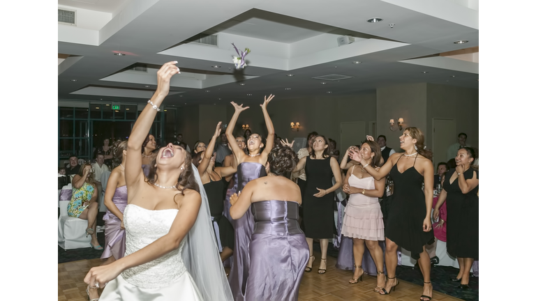 Bride tossing bouquet to bridesmaids in wedding reception