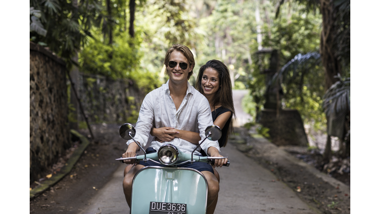 Young couple riding classic scooter during vacation in Bali