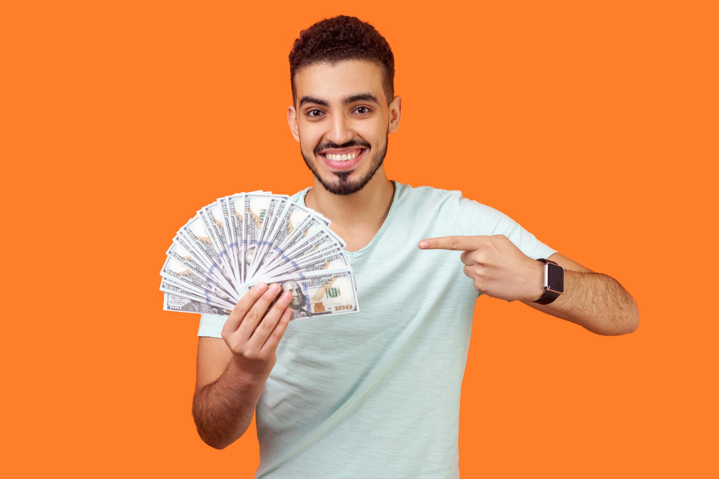 Portrait of lucky rich brunette man pointing at dollar banknotes. indoor studio shot isolated on orange background