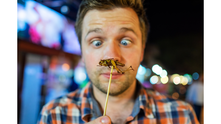 Caucasian young male eating cricket at night market in Thailand.