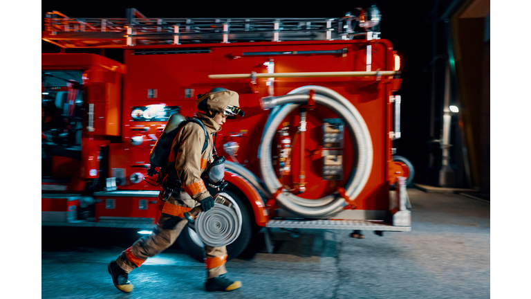 Firefighter running with a hose next to a fire engine