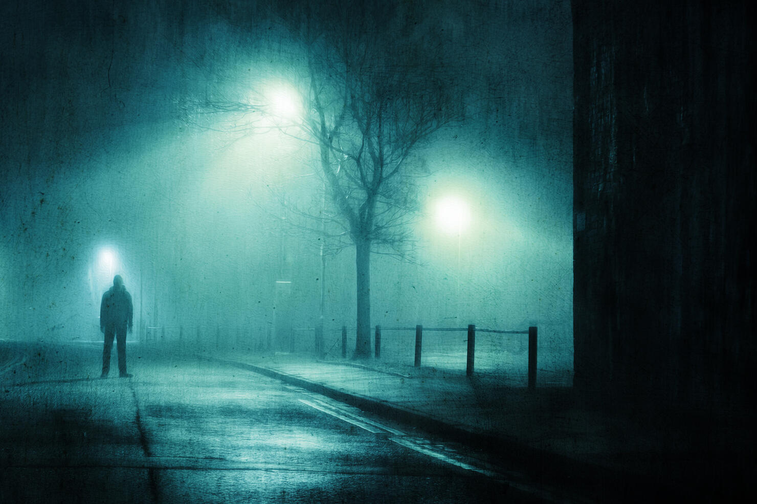 A moody figure. Standing in a street in a city on a foggy winters night. With a grunge, artistic, edit