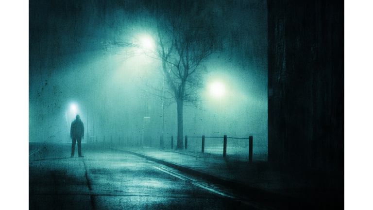 A moody figure. Standing in a street in a city on a foggy winters night. With a grunge, artistic, edit