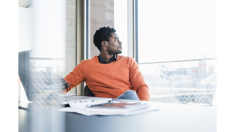 Casual businessman sitting at desk looking out of window