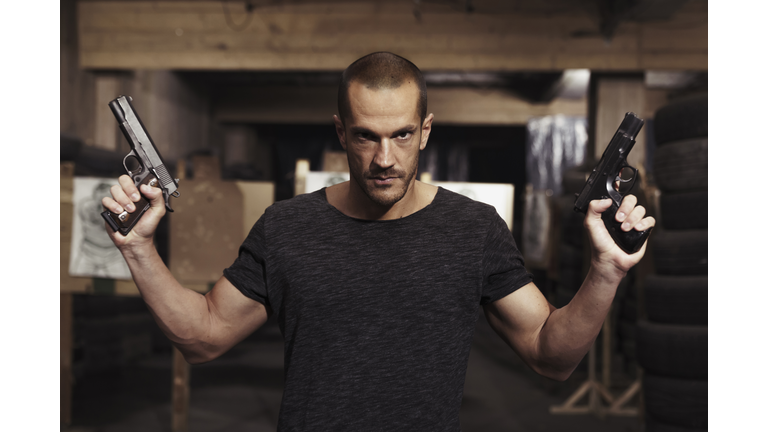 Portrait of man posing with two guns in an indoor shooting range