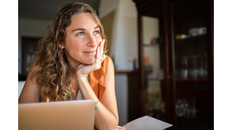 A woman with a dreamy expression working with a laptop from home