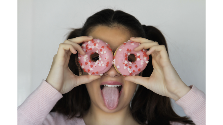 Funny beauty girl looking through two pink donuts. Diet, dieting concept. Junk food, Slimming, weight loss