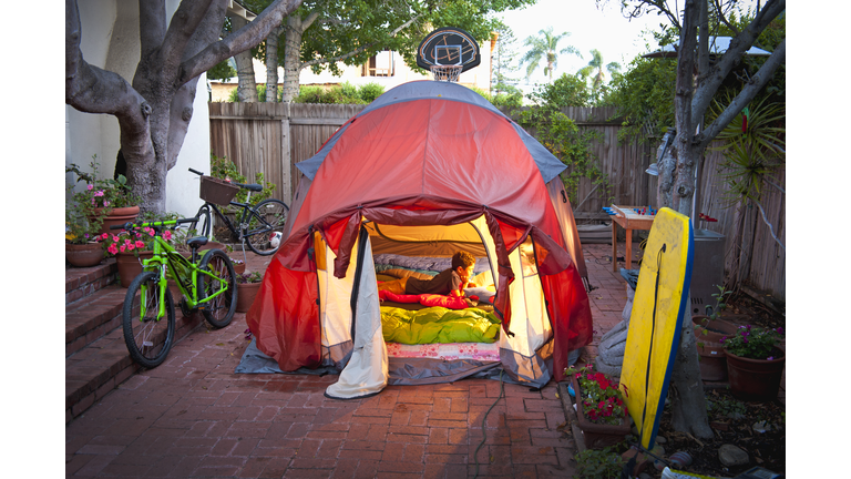 boy reading in tent in side yard of house