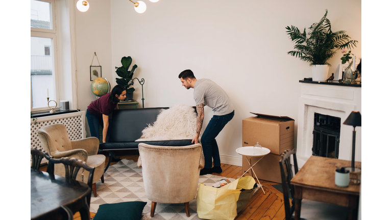 Man and woman arranging sofa in living room