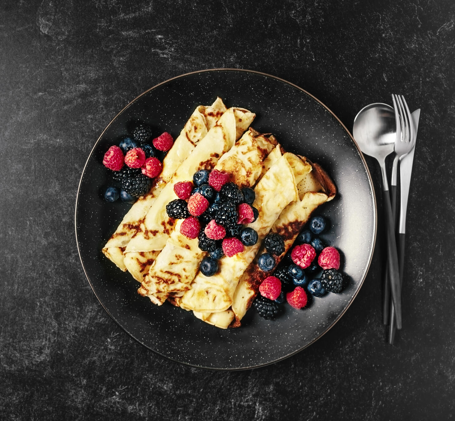 Plate of crepes with berries on black background