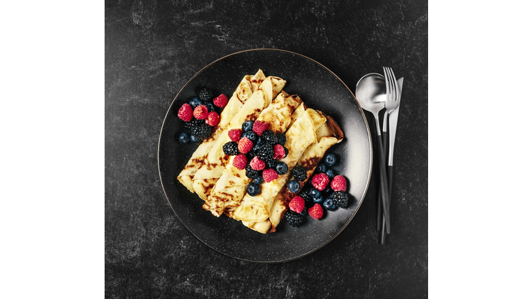 Plate of crepes with berries on black background