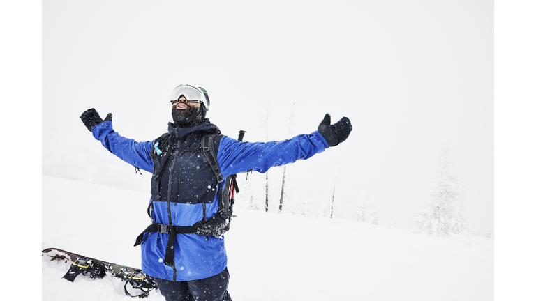 Man with outstretched arms enjoying snow storm while splitboarding in backcountry