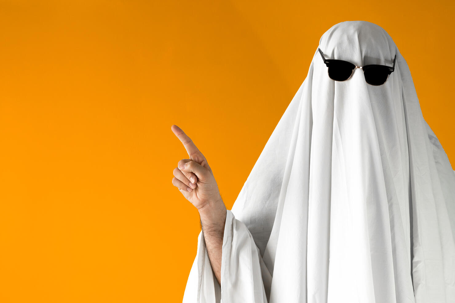 Person in Halloween costume of ghost with sunglasses points away
