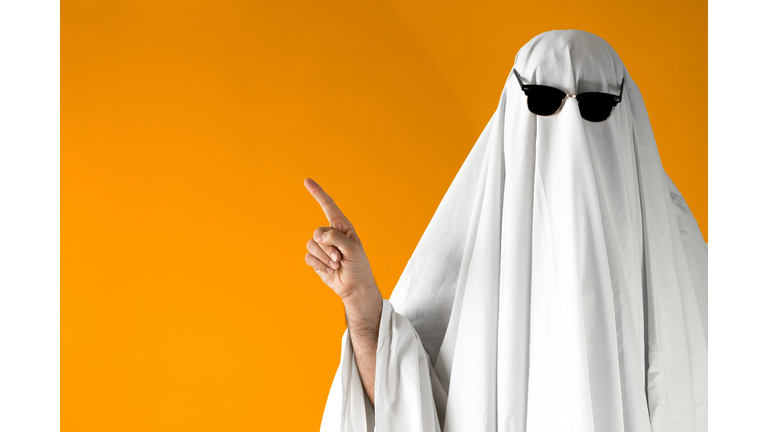 Person in Halloween costume of ghost with sunglasses points away