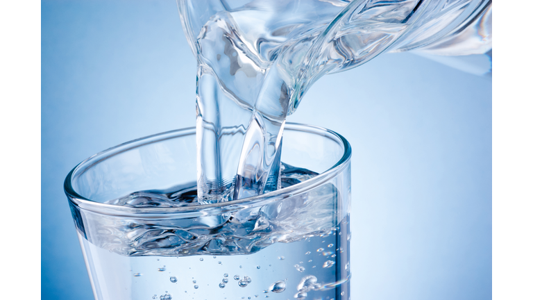 Pouring water from jug into glass on blue background