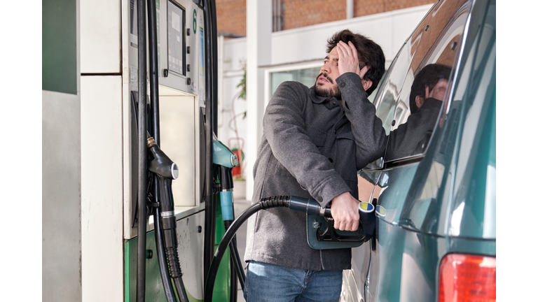 Young man refueling his vehicle while looking worried at the high gas prices.