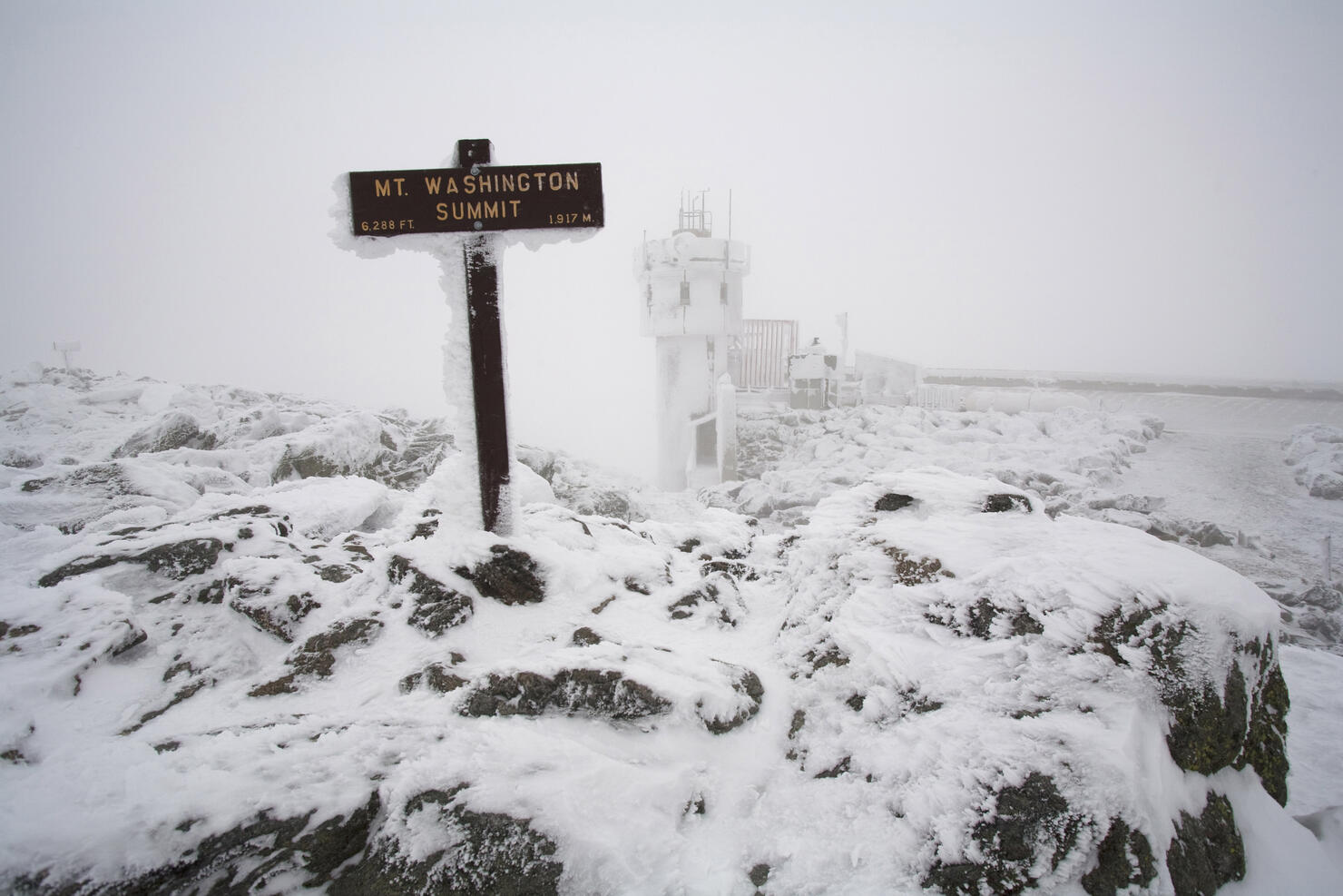 A snow and ice covered sign marks the summit of Mount Washington in the White Mountains of New Hamps