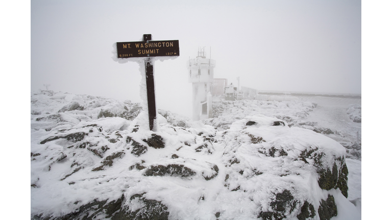 A snow and ice covered sign marks the summit of Mount Washington in the White Mountains of New Hamps