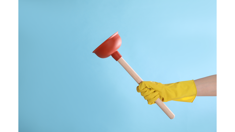 Woman holding plunger on turquoise background, closeup. Space for text