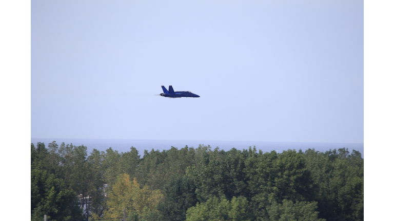 Military fighter jet aircraft in the air above trees.