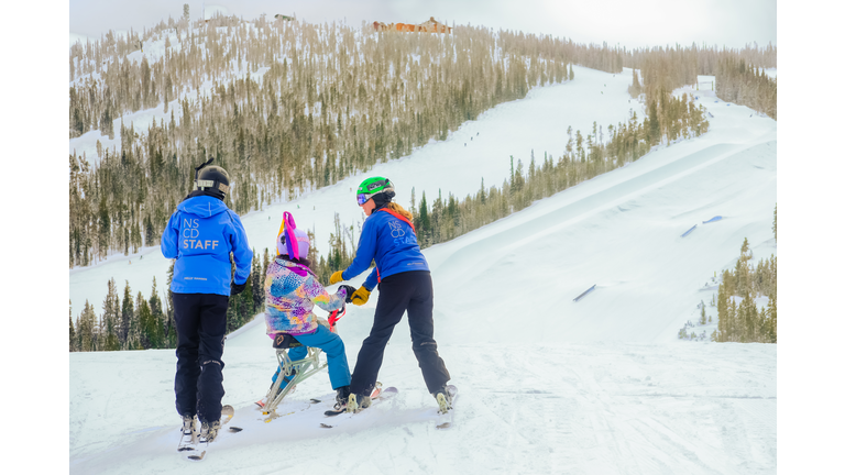 Two employees for National Sport Center for Disabled helping disabled girl in ski resort