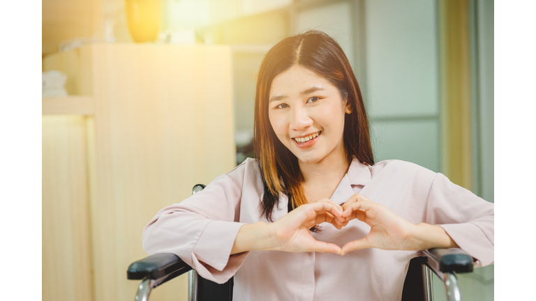 Happy Asian teen girl smile Heart shape hand sitting on wheelchair in hospital.