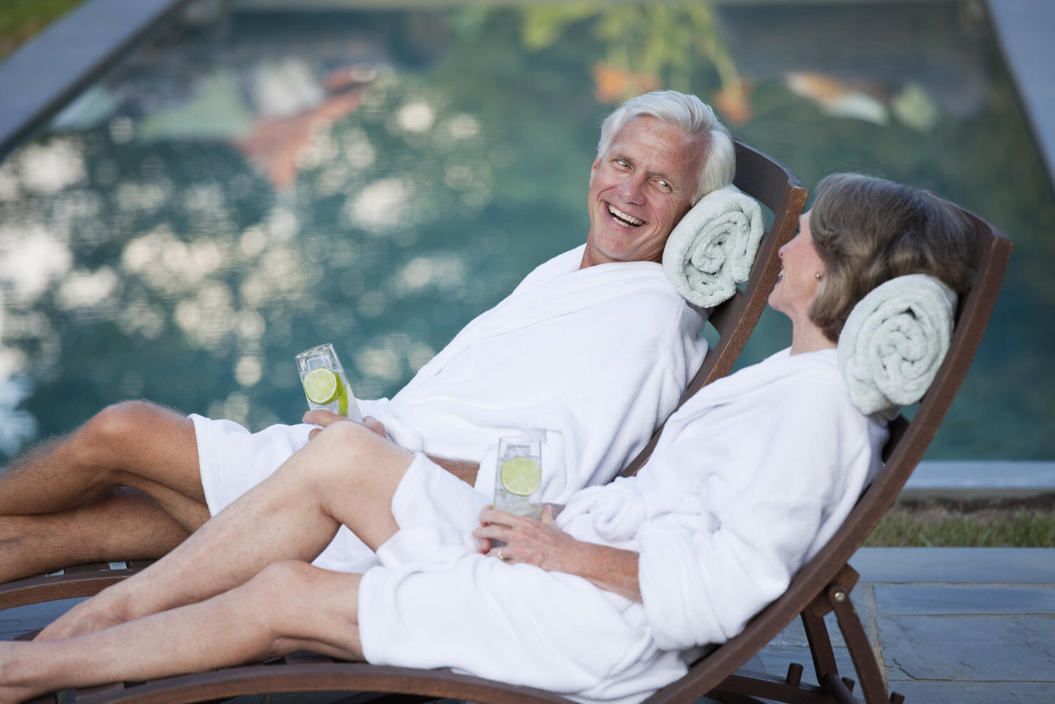 Couple in robes relaxing in lounge chairs at poolside