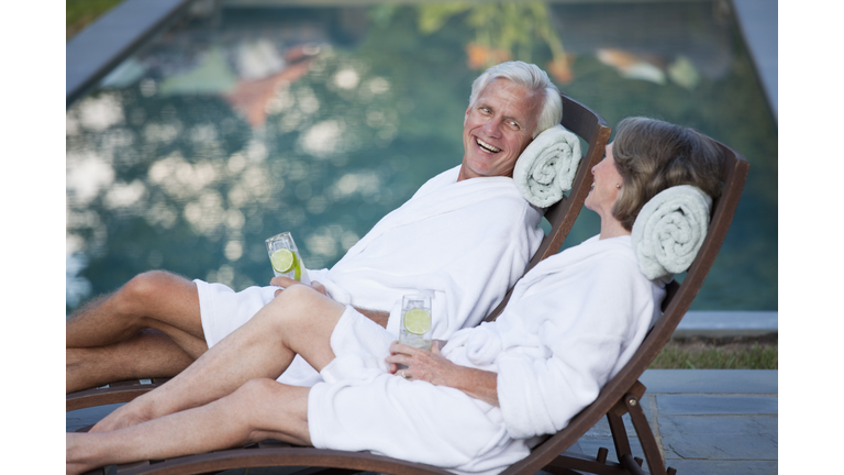 Couple in robes relaxing in lounge chairs at poolside