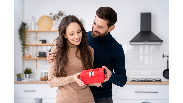 Loving husband surprising charming wife with present gift box on romantic day
