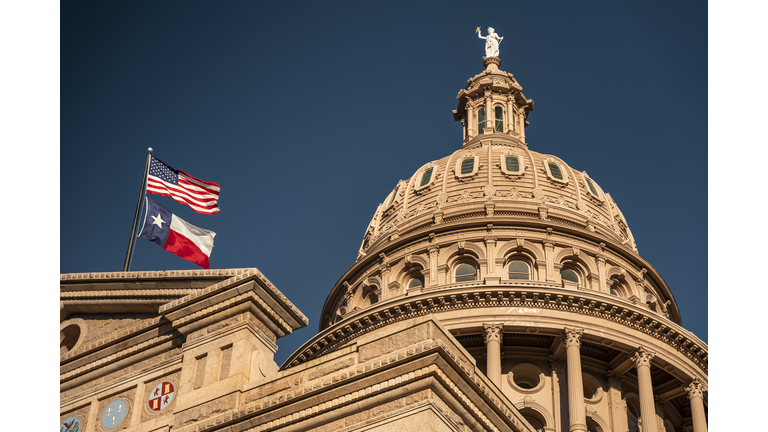 Pedestrians and traffic drive down Congress Avenue by the Texas State Capitol building in Austin