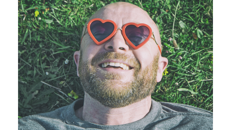 Man lying on the grass with red heart shaped sunglasses