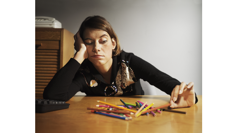 Woman at desk playing with coloured pencils, head in hand