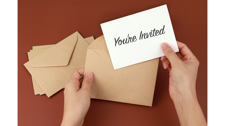 Cropped Hands Of Woman Holding Invitation Card On Brown Background