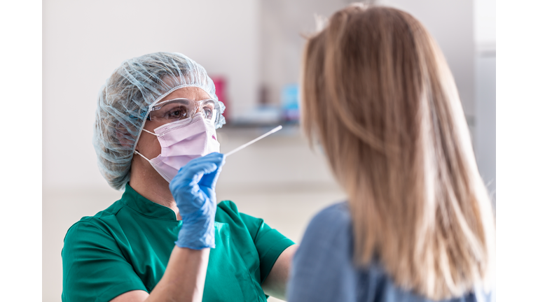 Well-protected medical staff performs swab test for Covid-19 to a young blonde female patient.