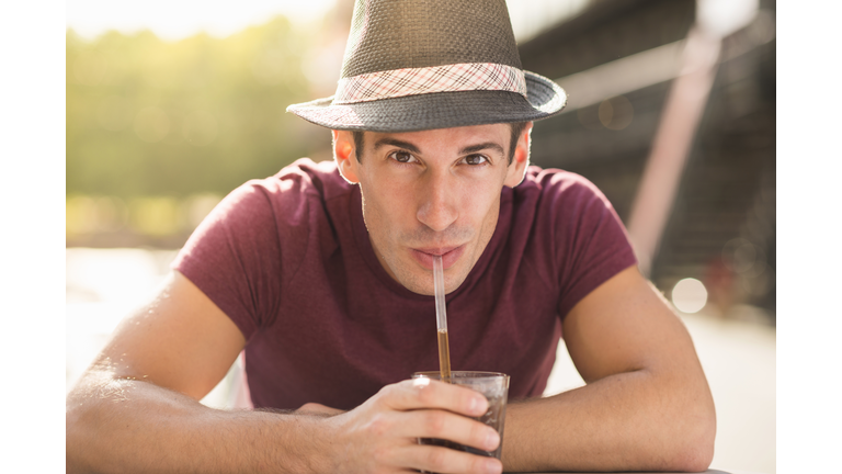 Young man wearing hat drinking through straw