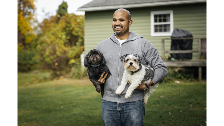 Mature man carrying dogs while standing at backyard